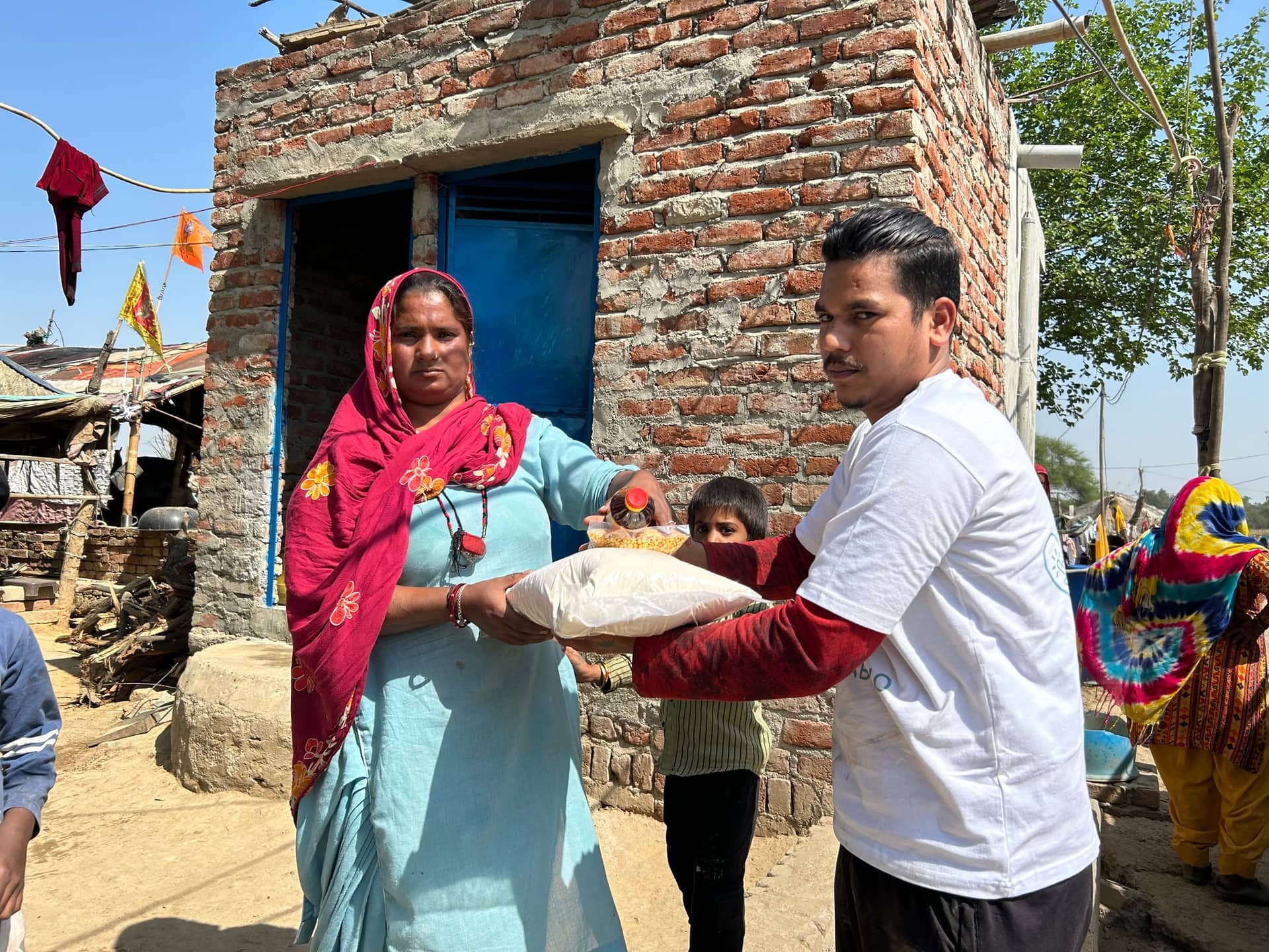 A Project Seva volunteer hands an atta sack and mustard-oil bottle to a woman outside her brick home in an informal settlement