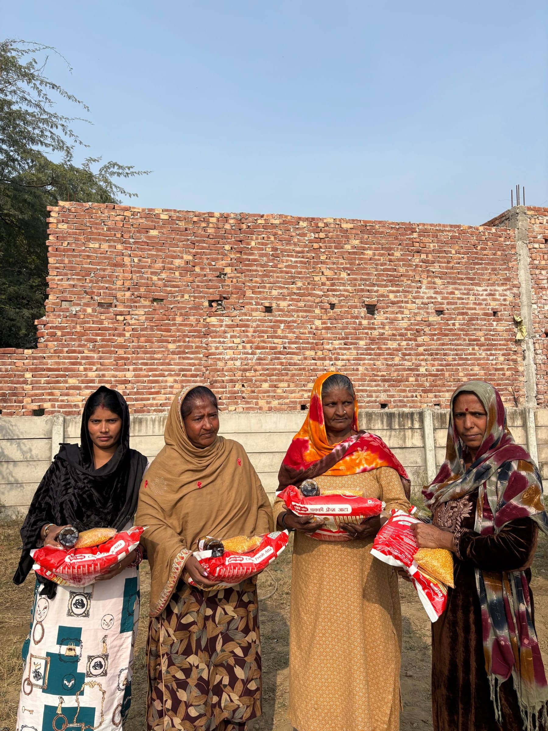 Line of women holding atta bags, brick building