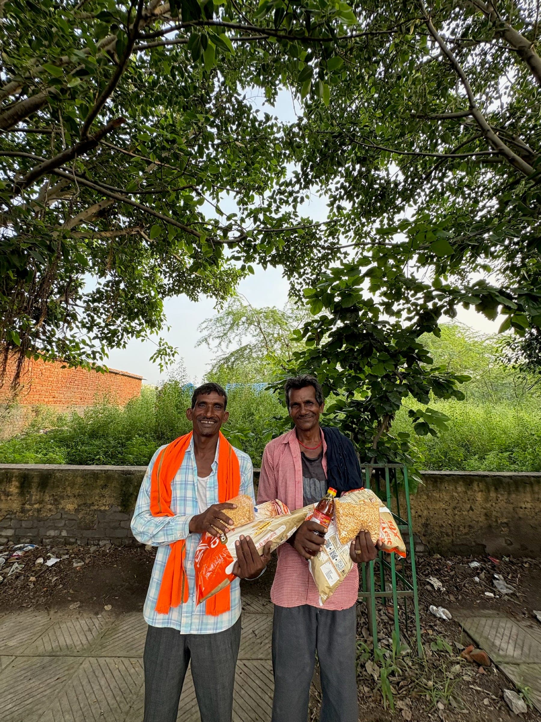 Two labourers smile under a green canopy holding their ration packets