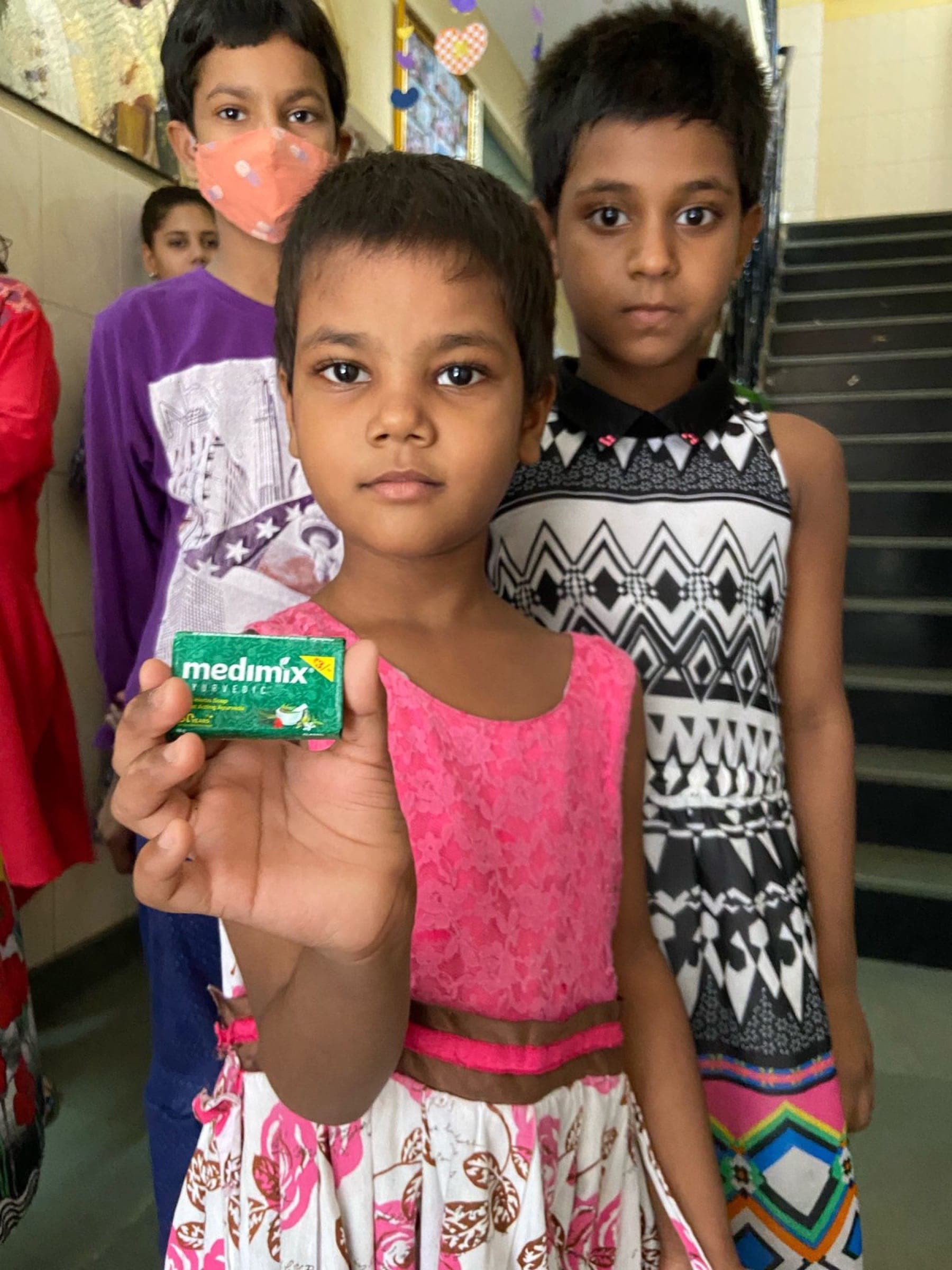 A girl holds up a soap bar from her Noori hygiene kit, looking straight at the camera
