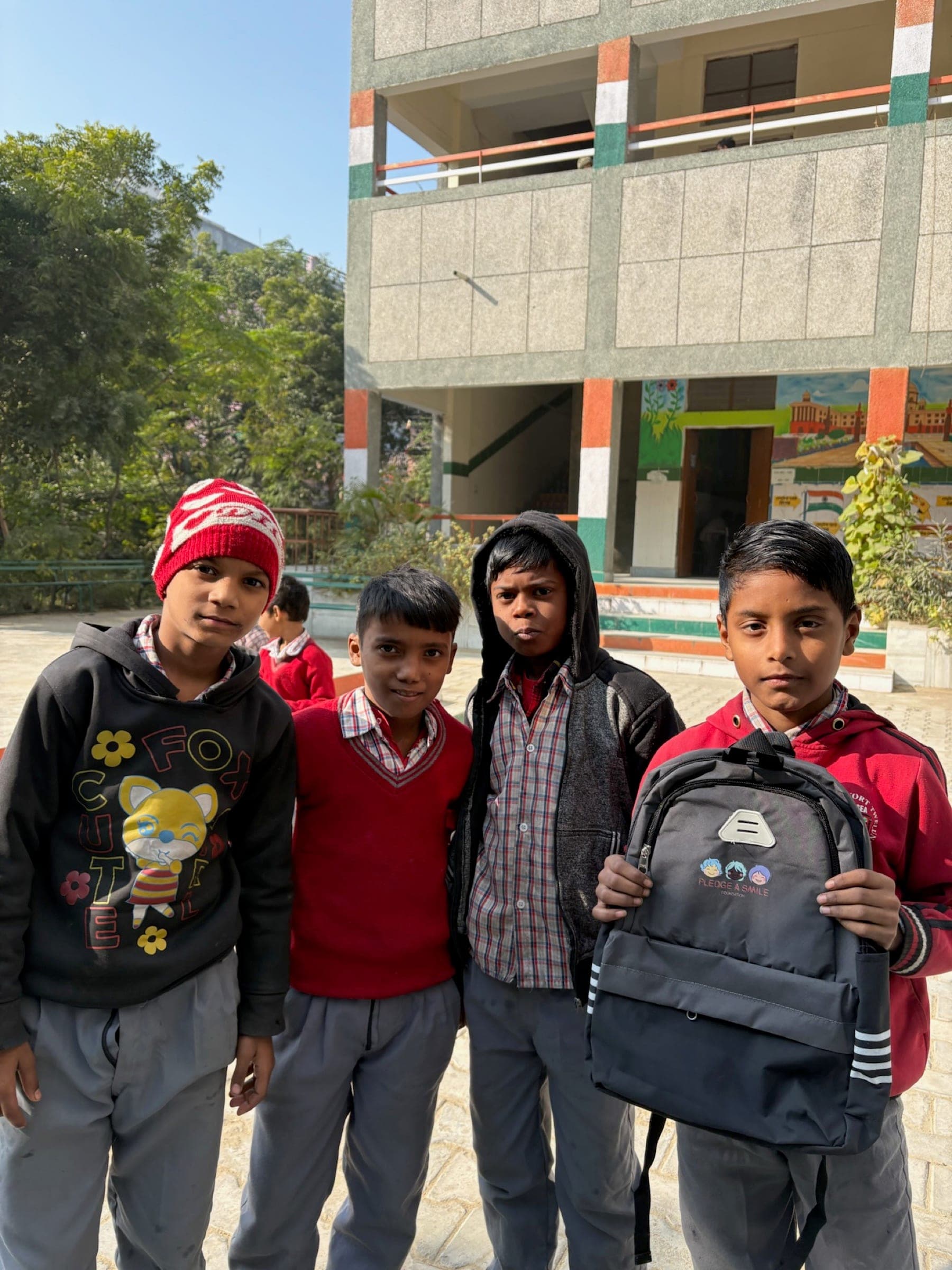 Four boys in winter wear show off a new backpack outside their school