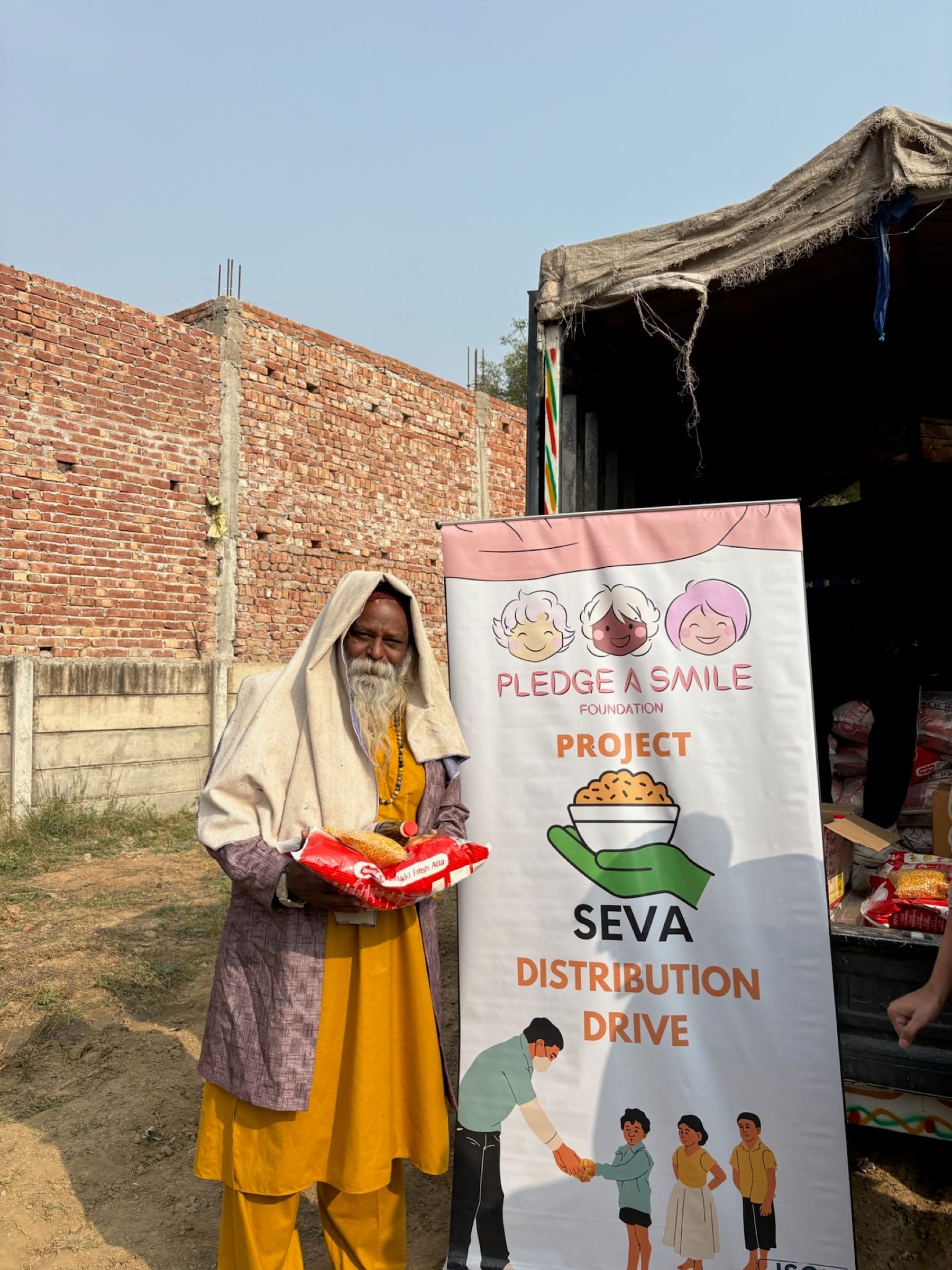 Elderly sadhu in saffron and white shawl receiving a ration kit