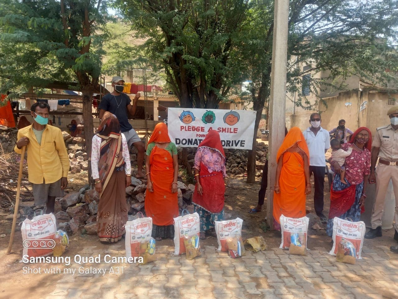 Five women in colourful saris stand behind their ration bags in a symmetric lineup, the banner behind.