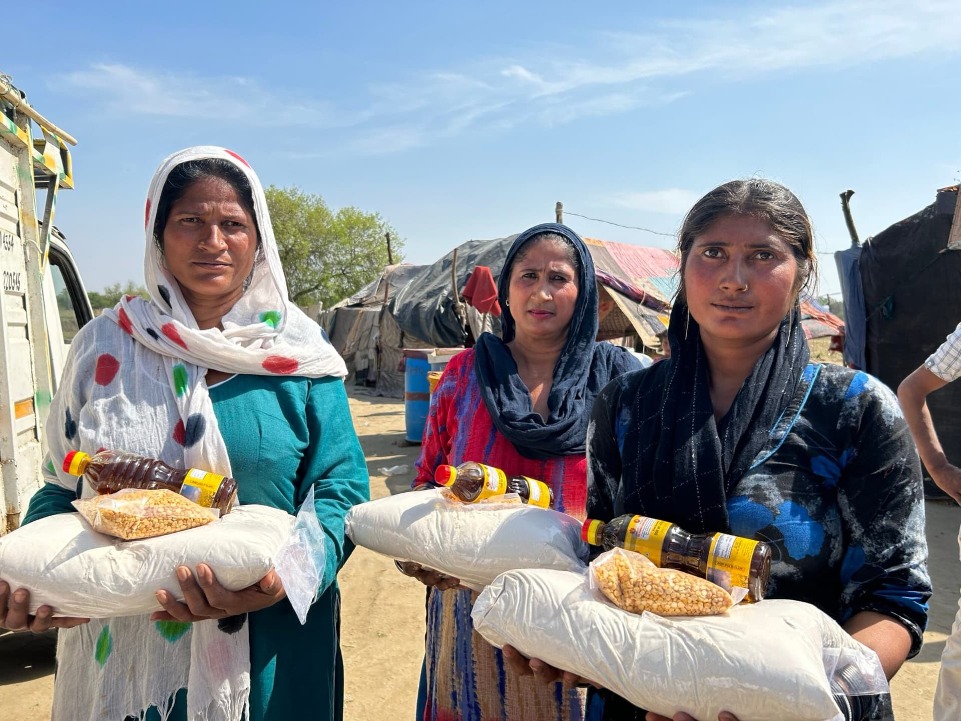 Three women hold ration sacks of dal and oil, looking straight into the camera